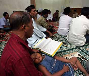 An Acehnese child sleeps as her father reads the Koran during a memorial service for last year's Indian Ocean tsunami victims in the district of Landung in Banda Aceh December 25, 2005.
